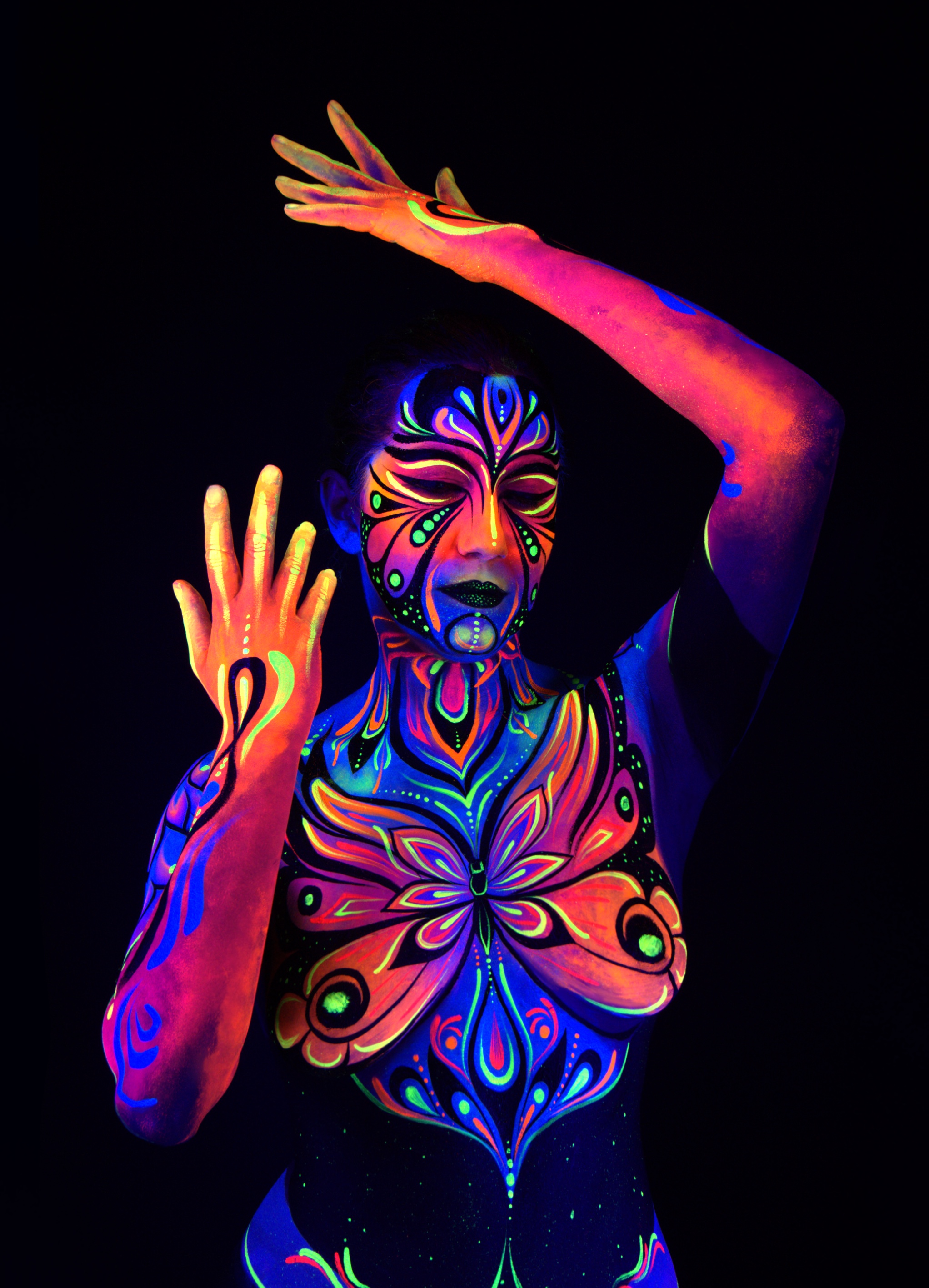 Katrina stands facing the camera in an upright pose. The bodypaint features a symmetrical butterfly design in pink, orange, and blue across the chest, with coordinating facial and body linework. Bodypaint by Joana Rohr. Photographed by Elad Itzkin Photography under UV light in his studio in Gesundbrunnen, Berlin.