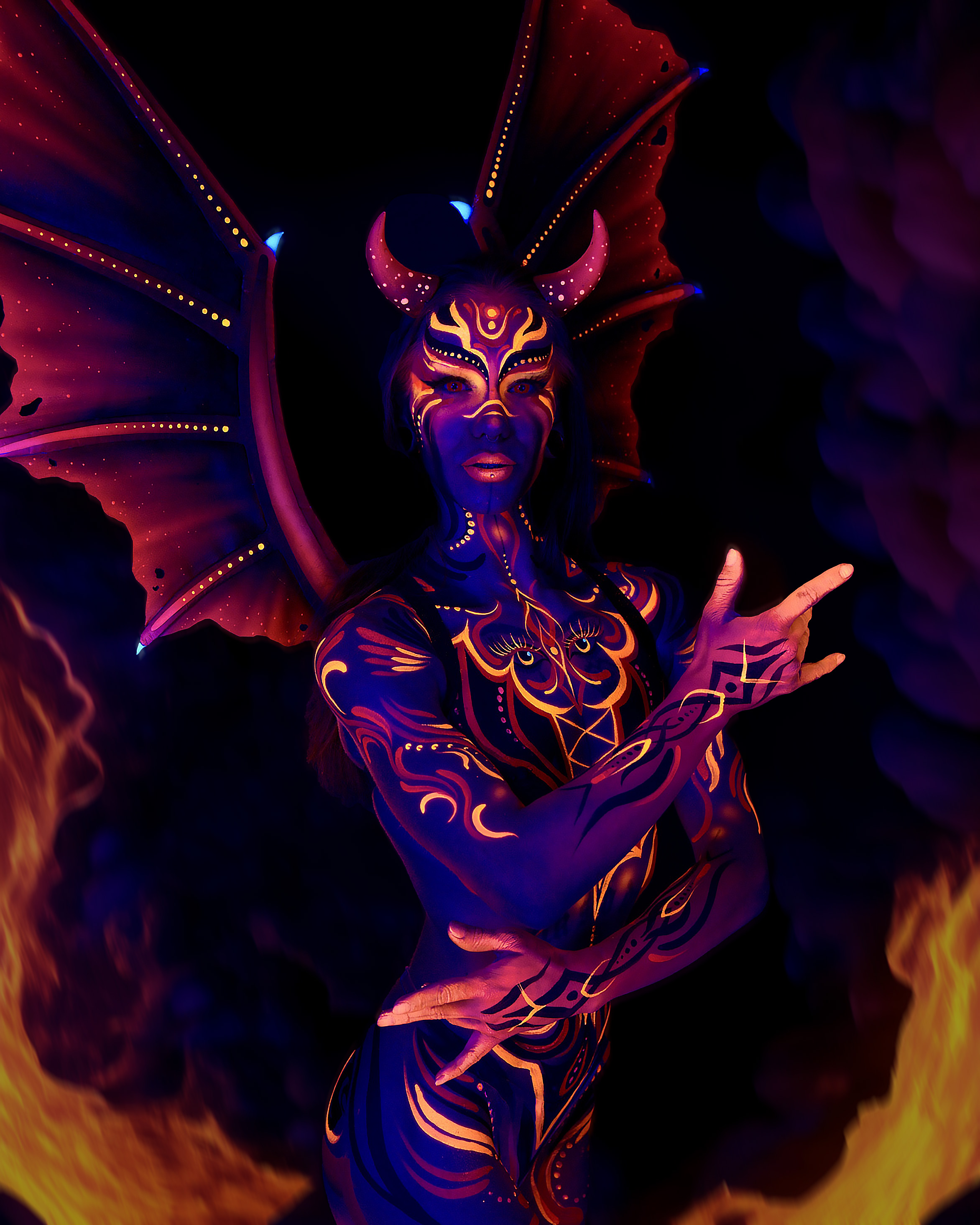 Thory stands facing the camera from the waist up, wearing a horned headpiece with wings extending from the shoulders. The chest and face are painted with an orange and purple symmetrical pattern that includes an eye-like motif. Bodypaint by Joana Rohr. Photographed by Elad Itzkin Photography under UV light in his Gesundbrunnen, Berlin studio.