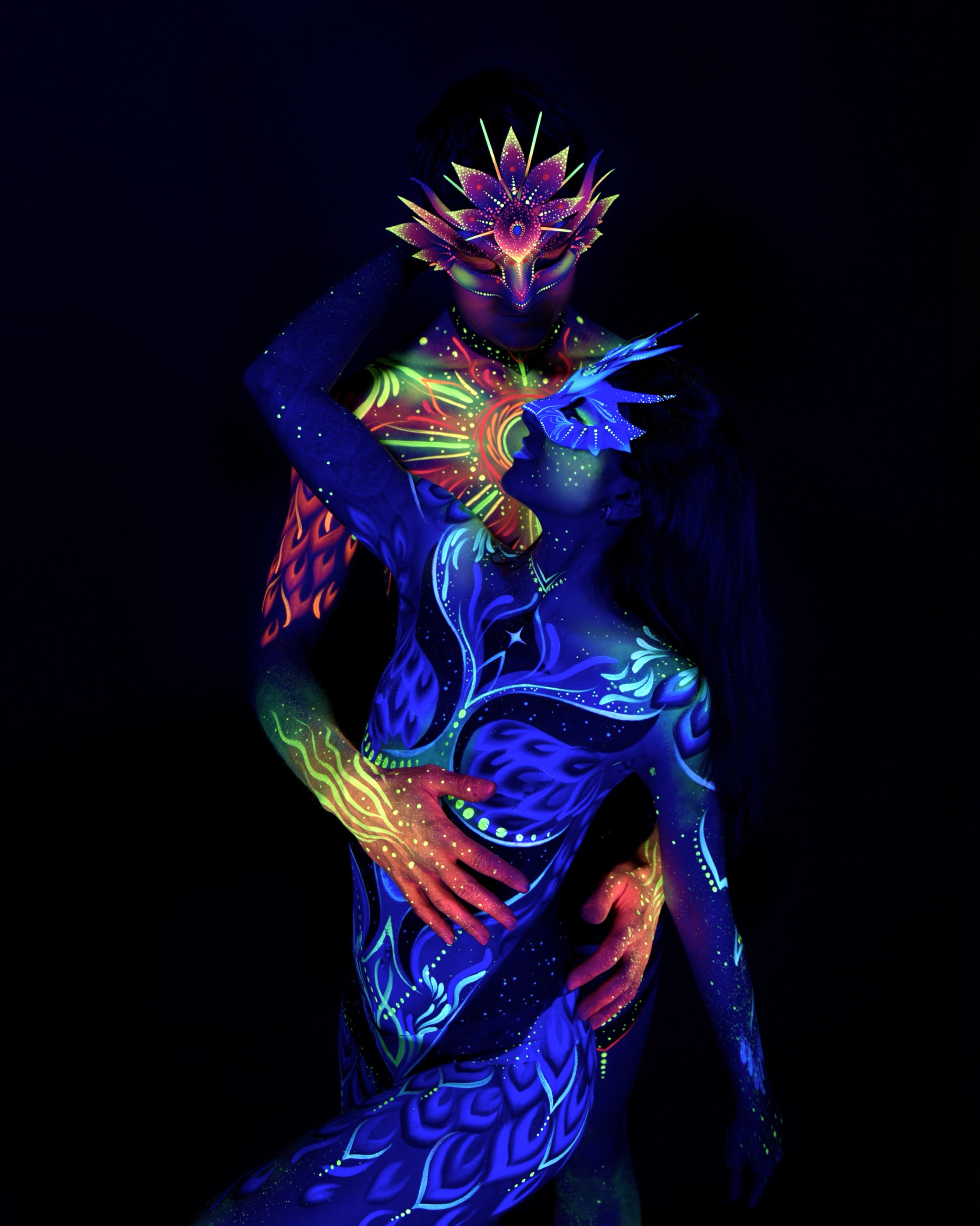 Sori and Julius are shown standing close together, Julius with his head tilted down and Sori facing upward toward him. Julius's chest carries an orange and green mandala design, while Sori wears a blue crown headpiece with matching linework. Bodypaint by Joana Rohr. Photographed by Elad Itzkin Photography under UV light in his Gesundbrunnen, Berlin studio.