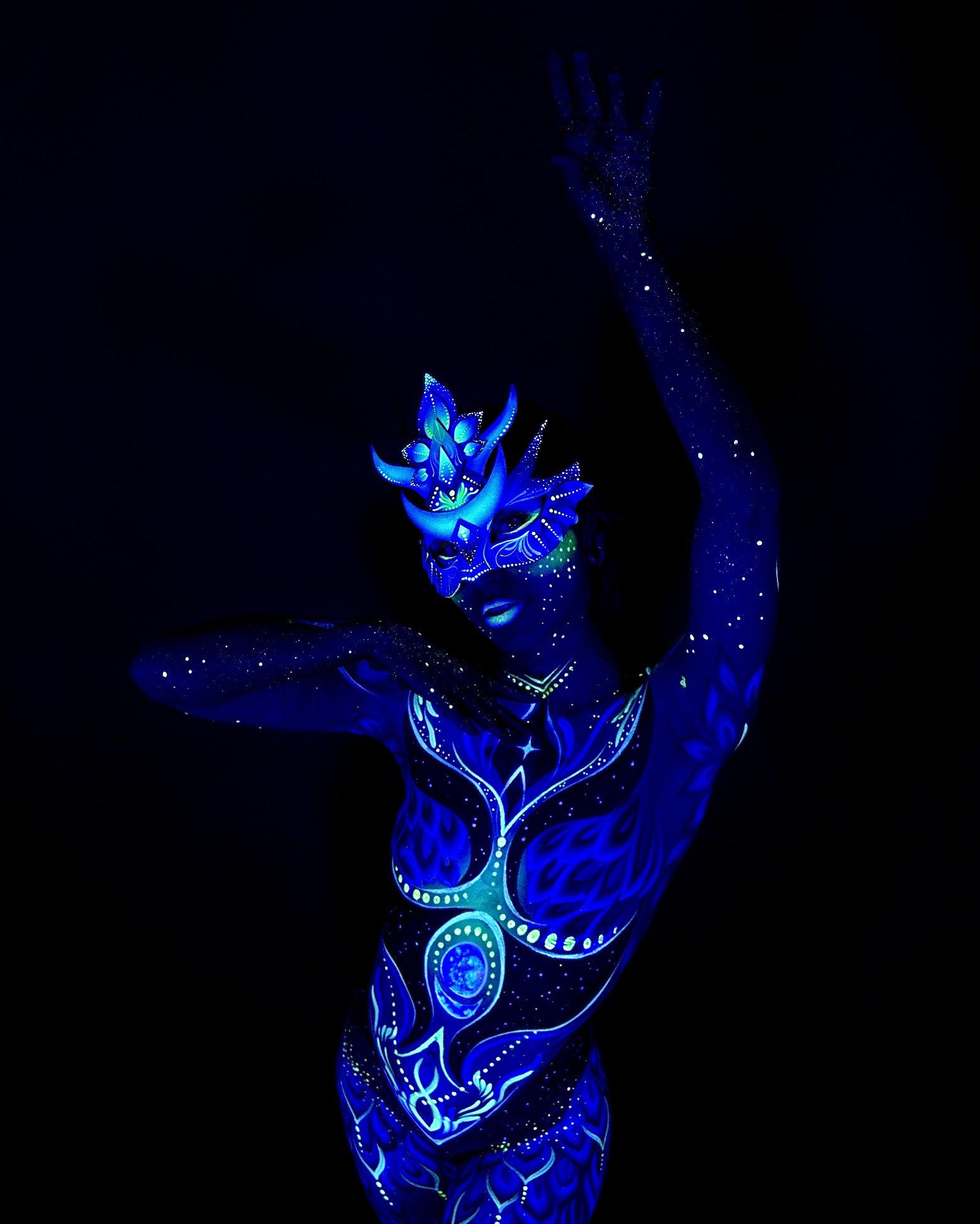 Sori stands in a three-quarter pose, body turned to one side and head angled toward the camera. She wears a blue crown-shaped headpiece, with a blue geometric pattern extending down the torso. Bodypaint by Joana Rohr. Photographed by Elad Itzkin Photography under UV light in his Gesundbrunnen, Berlin studio.