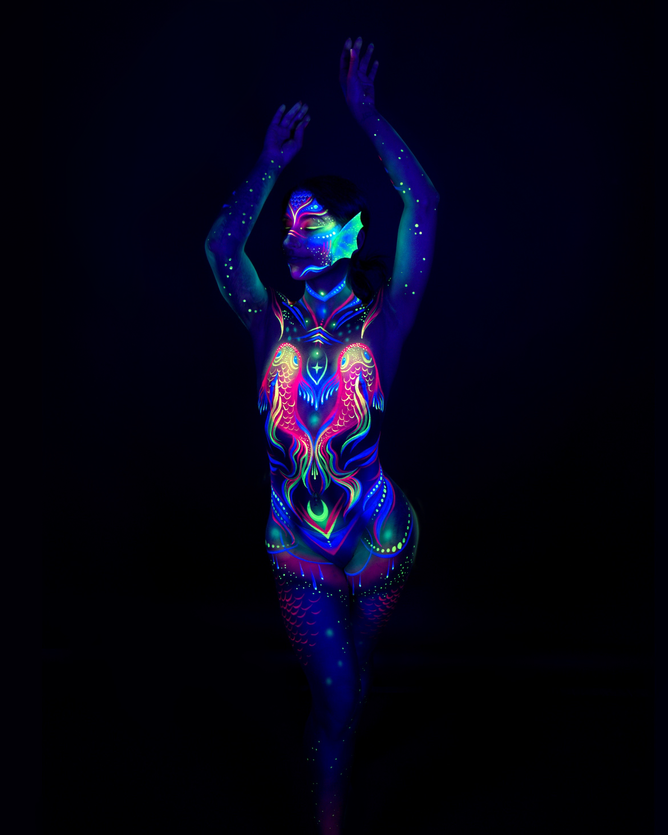 Sori stands facing the camera, head tilted back slightly. The bodypaint is an abstract linework design in pink, blue and green, with a mask-like pattern over the eyes and a geometric diamond motif on the lower body. Bodypaint by Joana Rohr. Photographed by Elad Itzkin Photography under UV blacklight in his studio in Gesundbrunnen, Berlin.