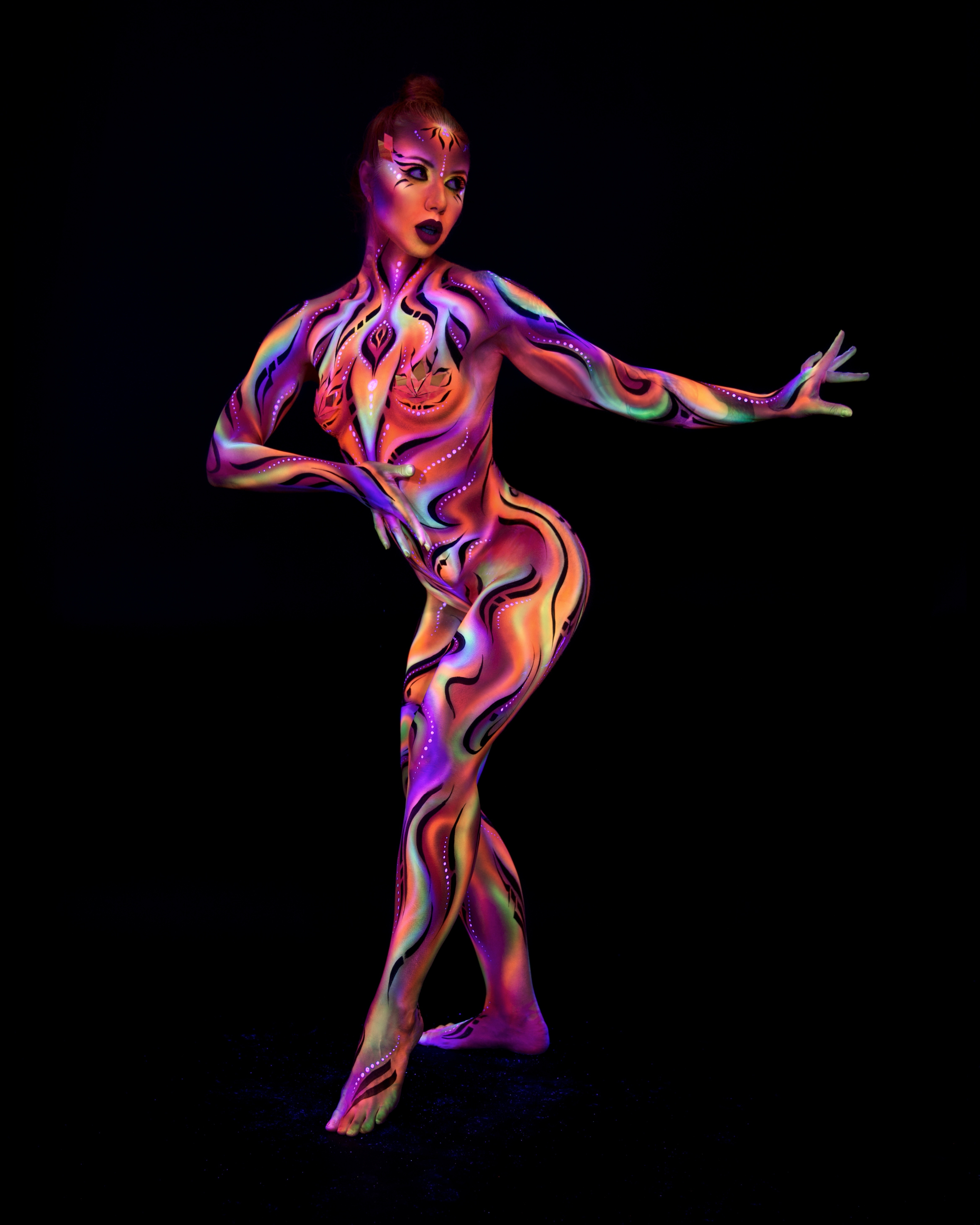 Irina stands in a three-quarter pose facing the camera. The full-body bodypaint is a swirling marbled pattern in orange, purple and teal, with a geometric design painted across the face. Bodypaint by Joana Rohr and Zami. Photographed by Elad Itzkin Photography under UV light in his studio in Gesundbrunnen, Berlin.