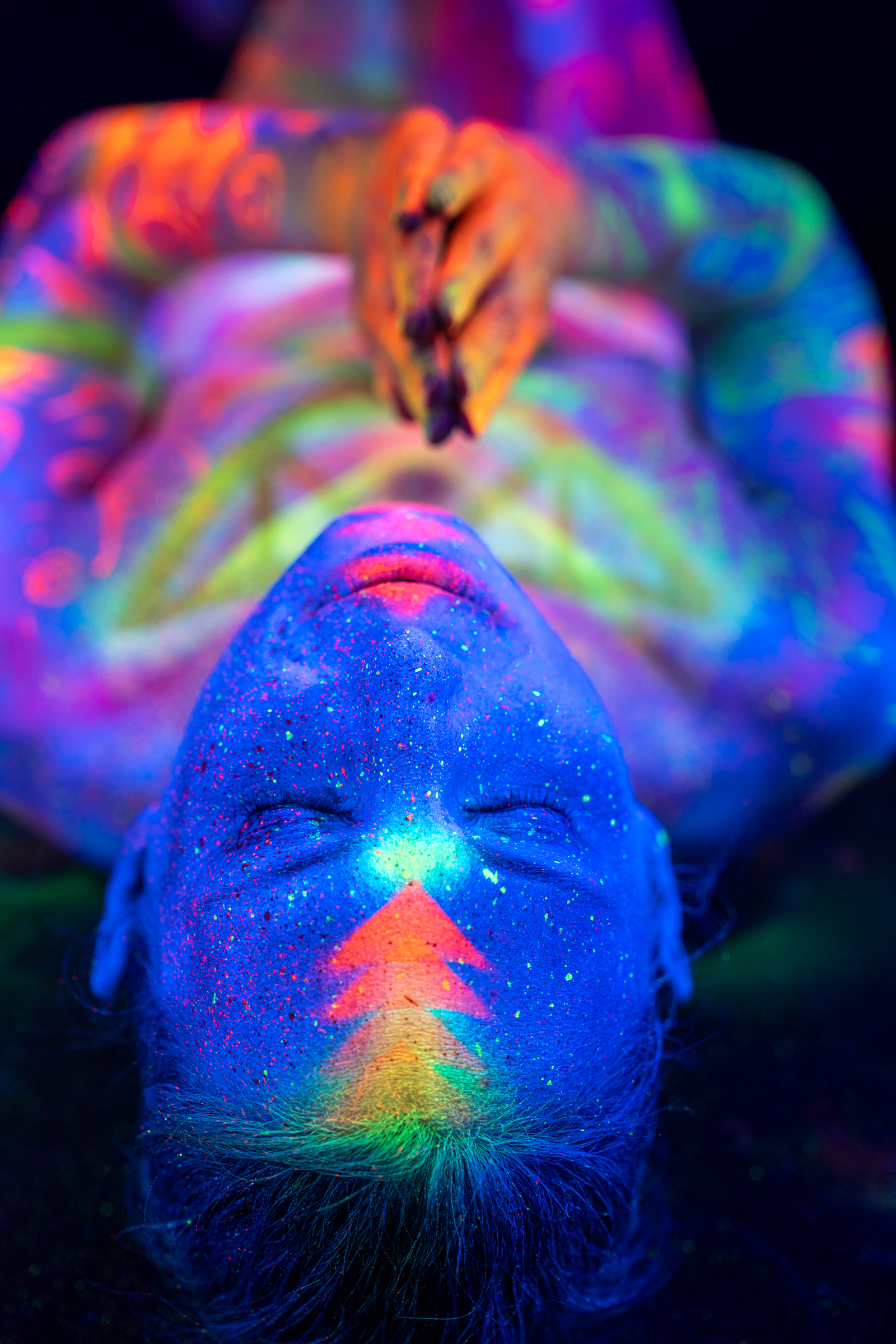 Alessia lies on the floor with her knees bent, photographed close up with her head at the base of the frame. Her legs and torso display a mix of scrollwork and geometric UV patterns. Bodypaint by Elad Itzkin, Geli. Photographed by Elad Itzkin Photography under UV light in Gesundbrunnen, Berlin.