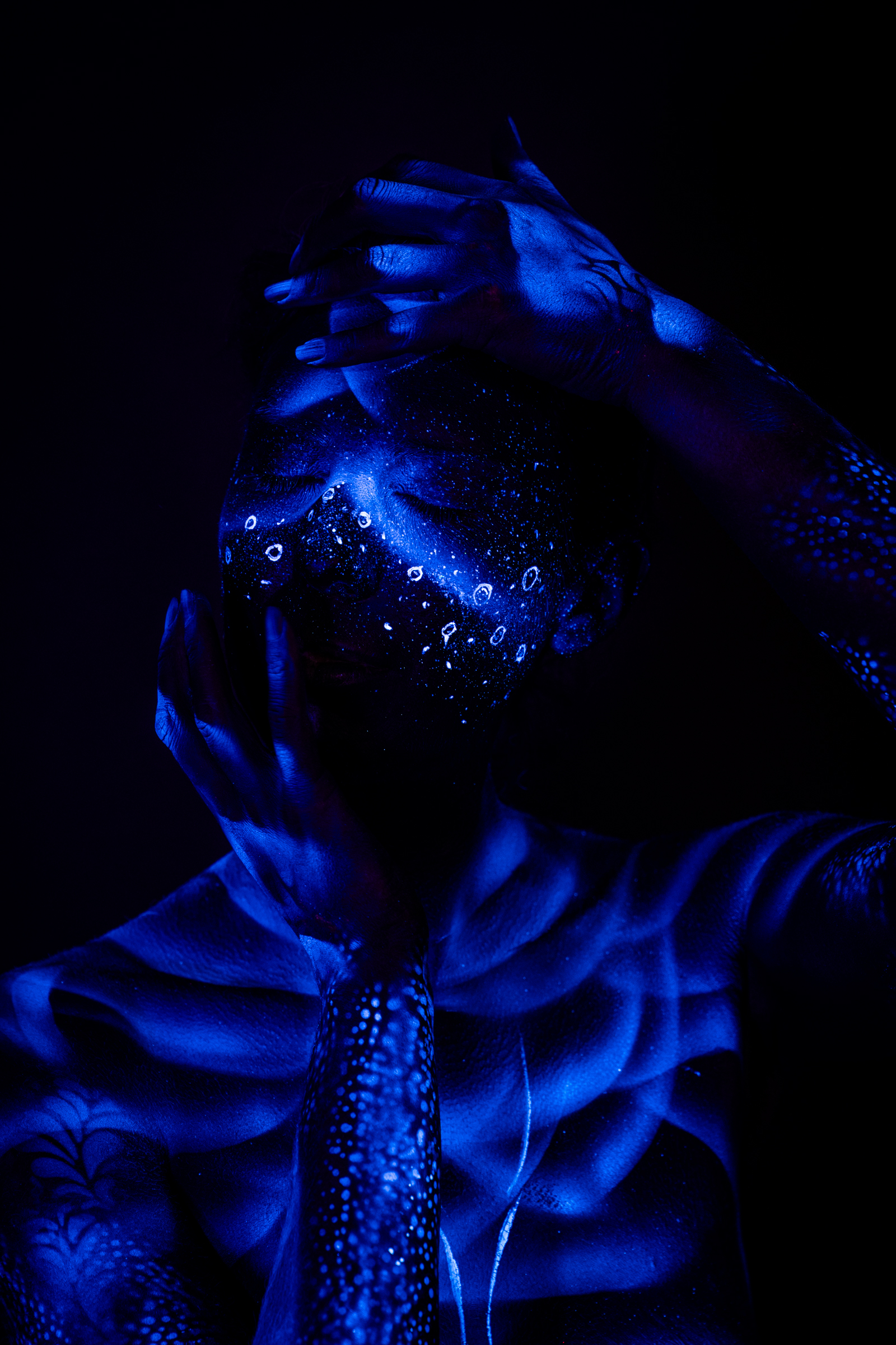 This front-facing shot shows Alessia standing, her torso marked with ribbed shading and a red accent line along one side. Her face carries a sparkling dotted pattern under UV light. Bodypaint by Geli, Charlotte Bobineau, Axell and Sage Brewer. Photographed by Elad Itzkin Photography in his studio in Gesundbrunnen, Berlin.