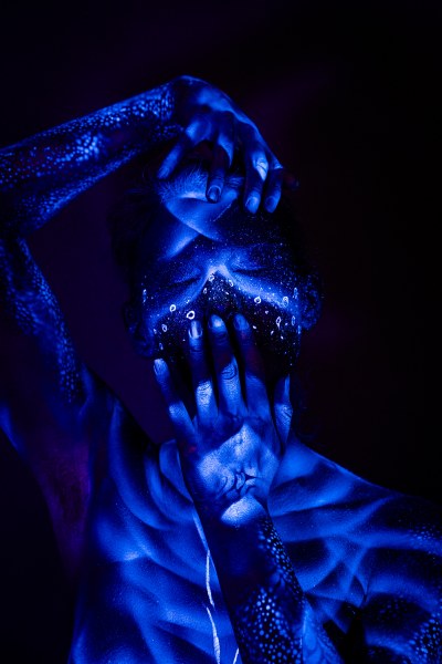 Alessia stands facing the camera, her torso showing ribbed shading that transitions into an abstract branching design on her lower abdomen. Bodypaint by Geli, Charlotte Bobineau, Axell and Sage Brewer. Photographed by Elad Itzkin Photography under UV light in his Gesundbrunnen, Berlin studio.