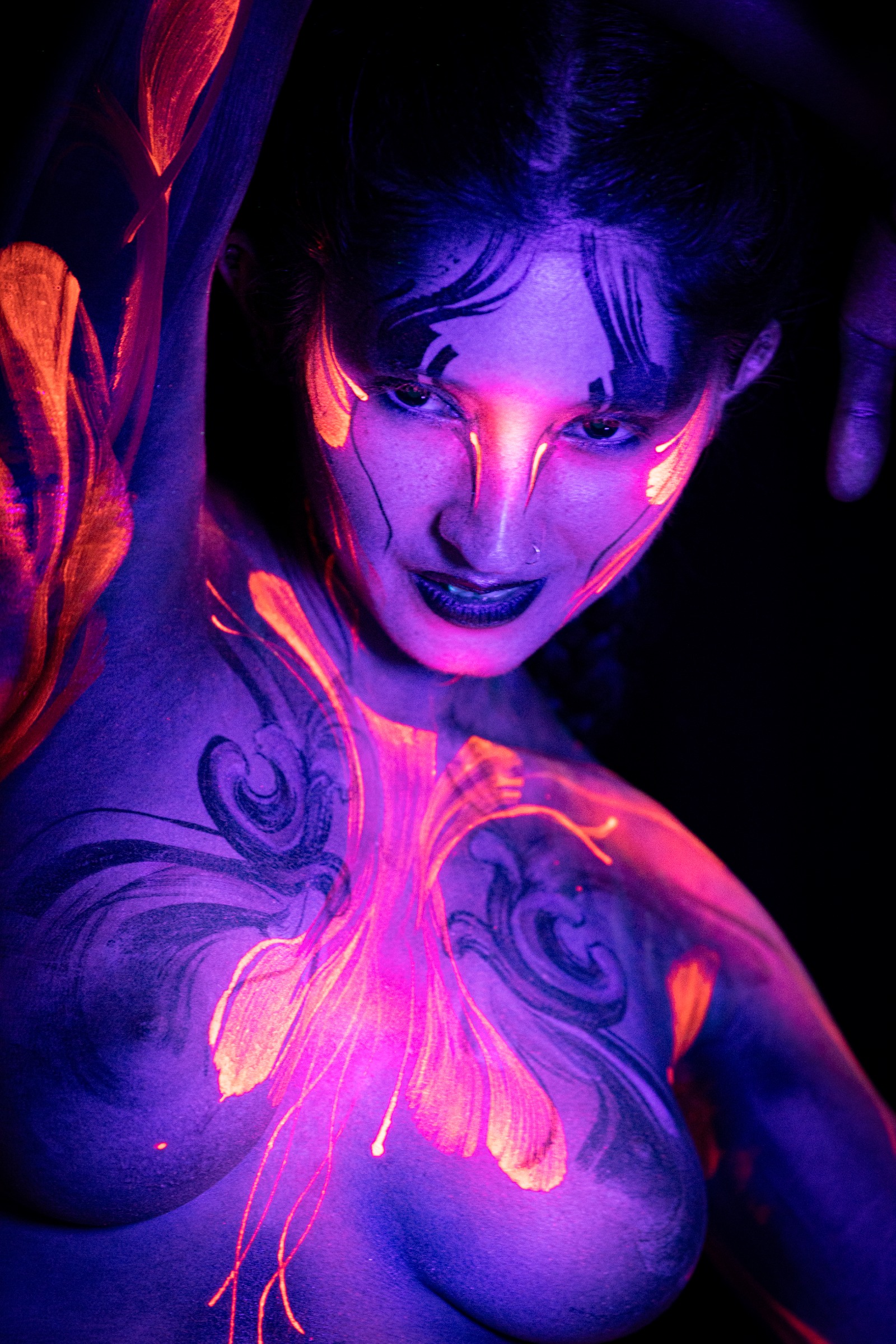 BabeyGianna stands in a three-quarter view facing the camera, her deep purple UV-lit skin marked with an orange leaf and vine linework pattern running down one side of her torso. Bodypaint by Claudia Kraemer, photographed by Elad Itzkin Photography under UV light in his studio in Gesundbrunnen, Berlin.
