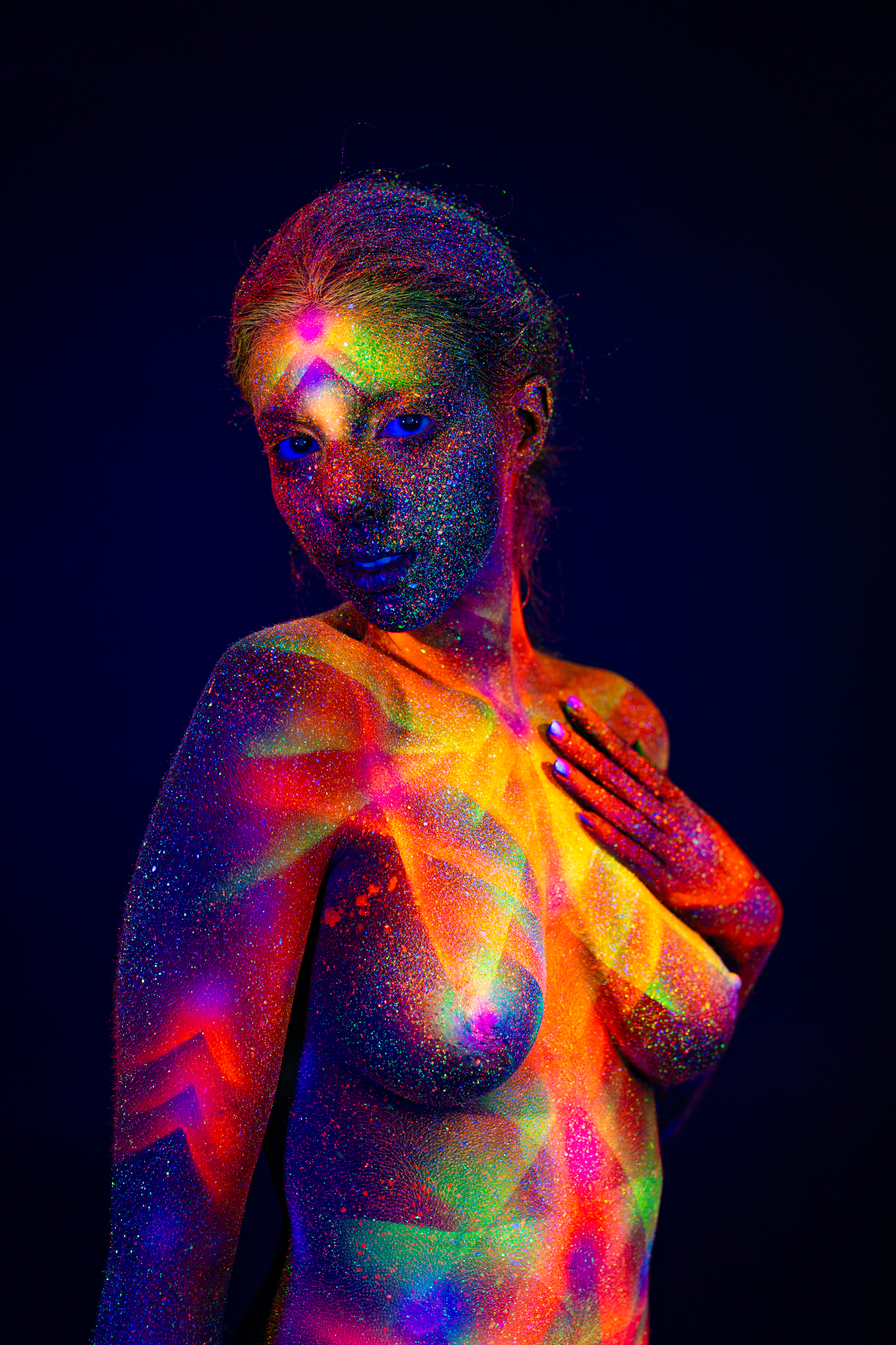 Sofia stands in profile with her head tilted back, her upper back and shoulder visible to the camera. A geometric pattern of dots and radiating lines glows across her back. Bodypaint by Elad Itzkin. Photographed by Elad Itzkin Photography under UV/blacklight in his studio in Gesundbrunnen, Berlin.