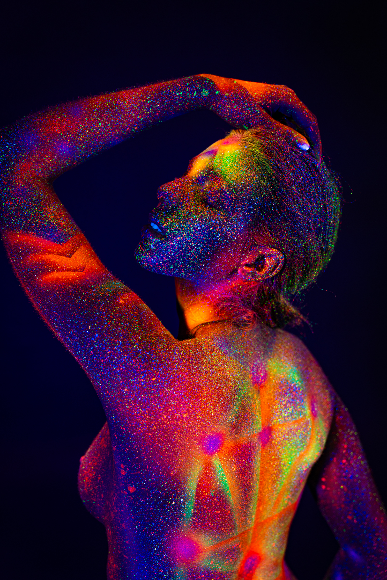 Sofia stands in profile view with her head tilted back and her face turned upward. A multicolor geometric design of radiating lines and dots covers her torso and back under UV light. Bodypaint by Elad Itzkin. Photographed by Elad Itzkin Photography under UV/blacklight in his studio in Gesundbrunnen, Berlin.
