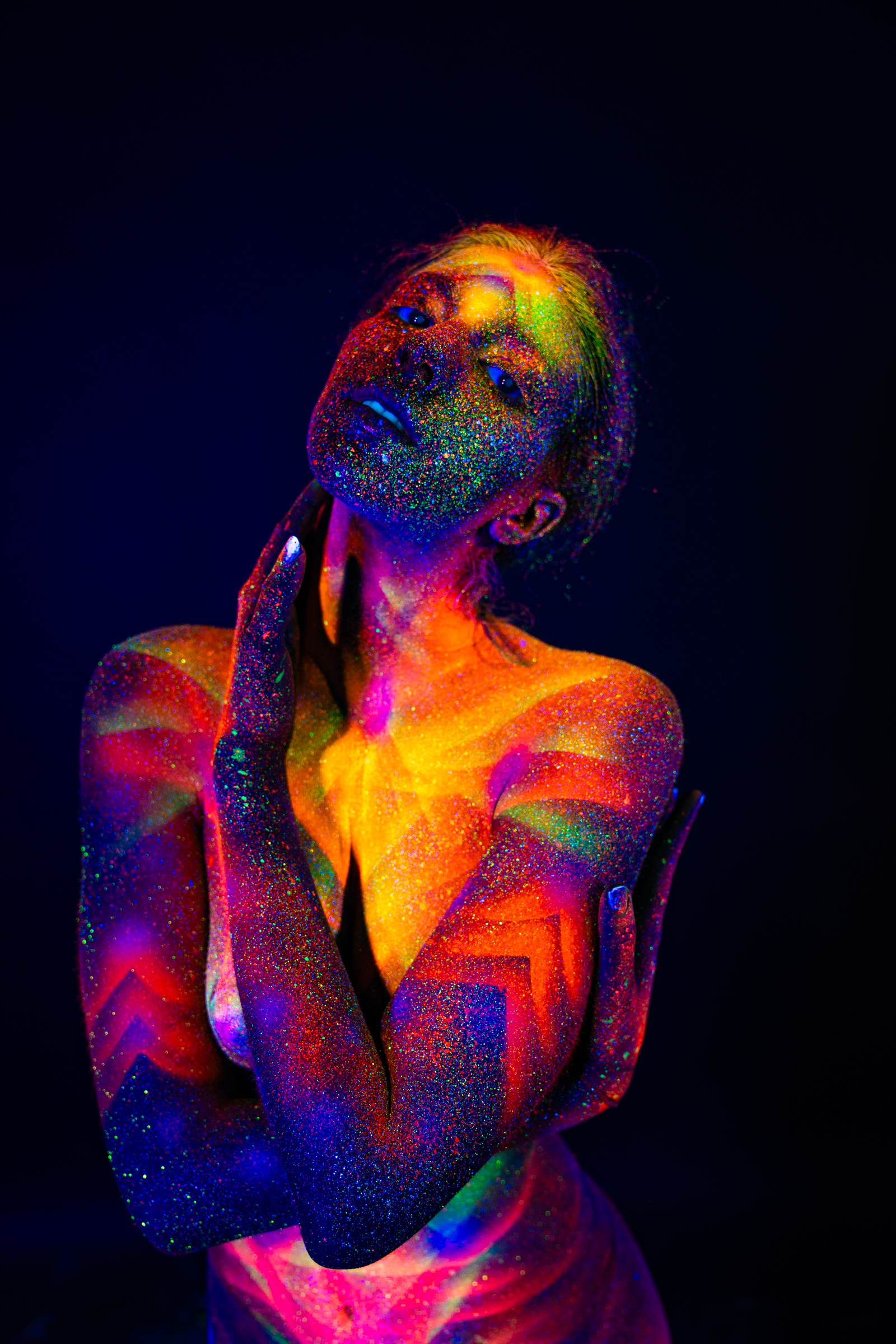 Sofia stands facing forward with her head tilted back. Her chest and torso carry a radiating geometric star pattern in orange and yellow, framed by chevron lines in blue. Bodypaint by Elad Itzkin. Photographed by Elad Itzkin Photography under UV light in his Berlin studio.