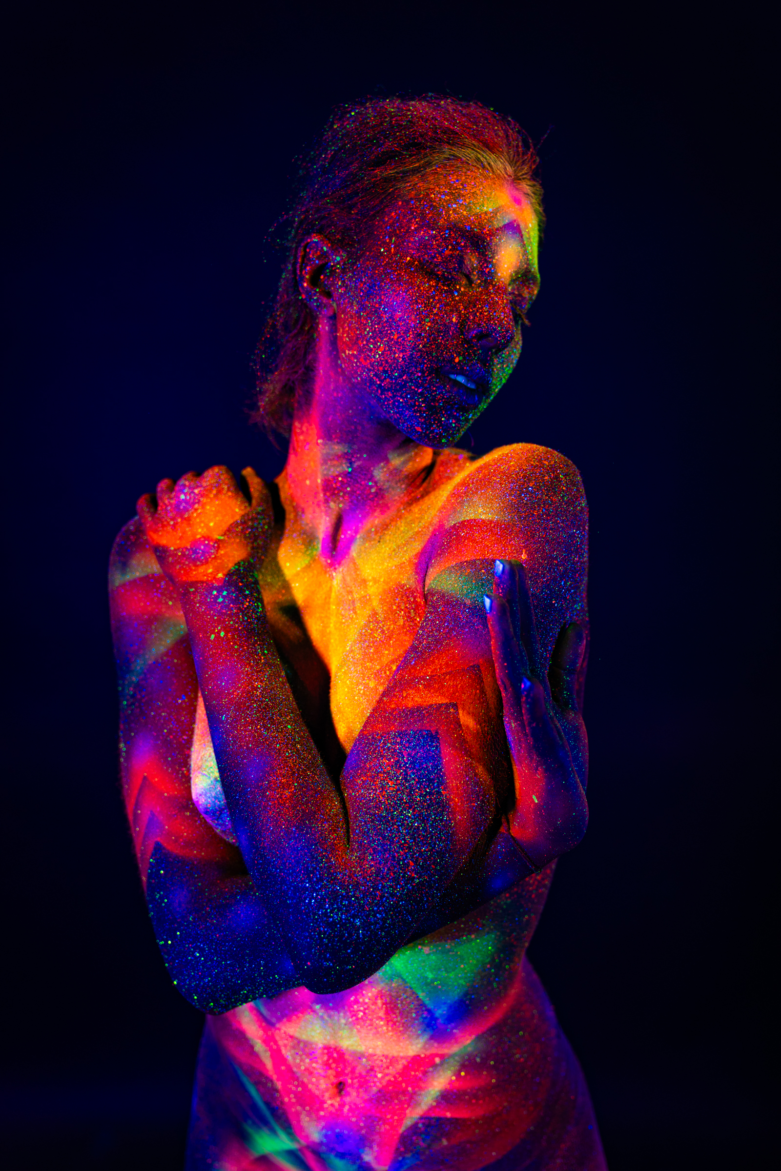 Sofia is photographed in a three-quarter view, her head turned slightly downward. A geometric pattern of chevrons and a radiating star design glows in orange and blue across her torso. Bodypaint by Elad Itzkin. Photographed by Elad Itzkin Photography under UV light in his Berlin studio.