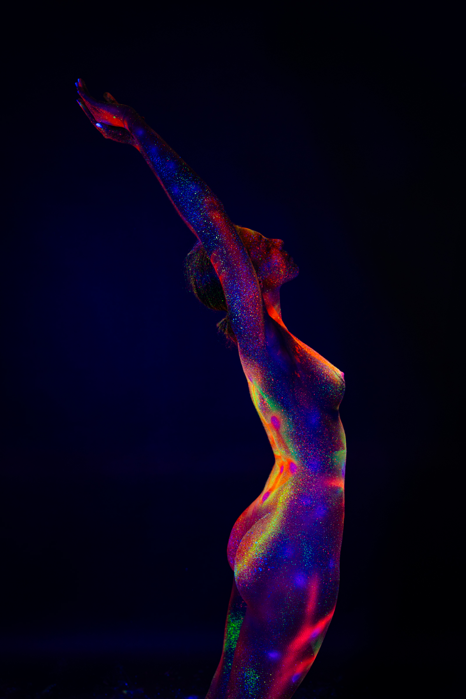 Sofia stands in profile, facing away from the camera. An abstract geometric linework design in blue, red, and green covers her torso. Bodypaint by Elad Itzkin. Photographed by Elad Itzkin Photography under UV light in his studio in Gesundbrunnen, Berlin.
