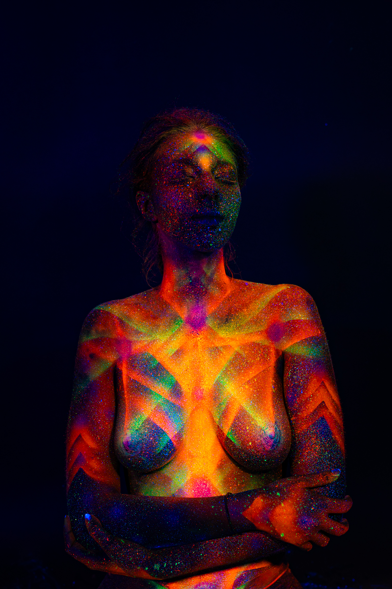 Sofia appears in a frontal portrait pose, facing the camera directly. A geometric linework pattern in orange, green, pink and blue radiates across her chest and shoulders. Bodypaint by Elad Itzkin. Photographed by Elad Itzkin Photography under UV light in his Gesundbrunnen, Berlin studio.