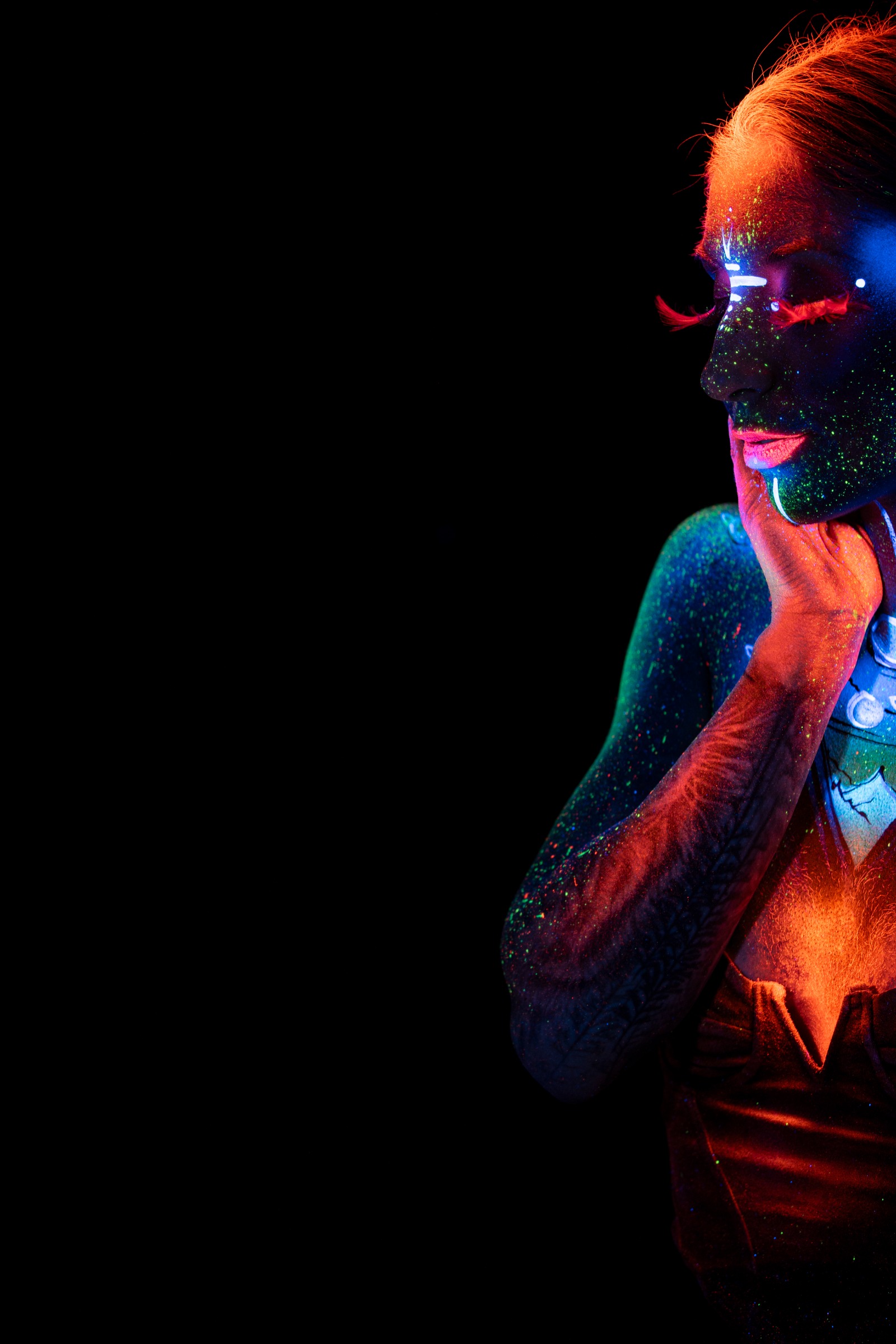 Sori is shown in profile, turned toward the side of the frame. Blue and orange tones form a space themed design with circular planet motifs on her chest and neck, paired with dark facial UV paint. Bodypaint by Claudia Kraemer. Photographed by Elad Itzkin Photography under UV light in his Gesundbrunnen, Berlin studio.